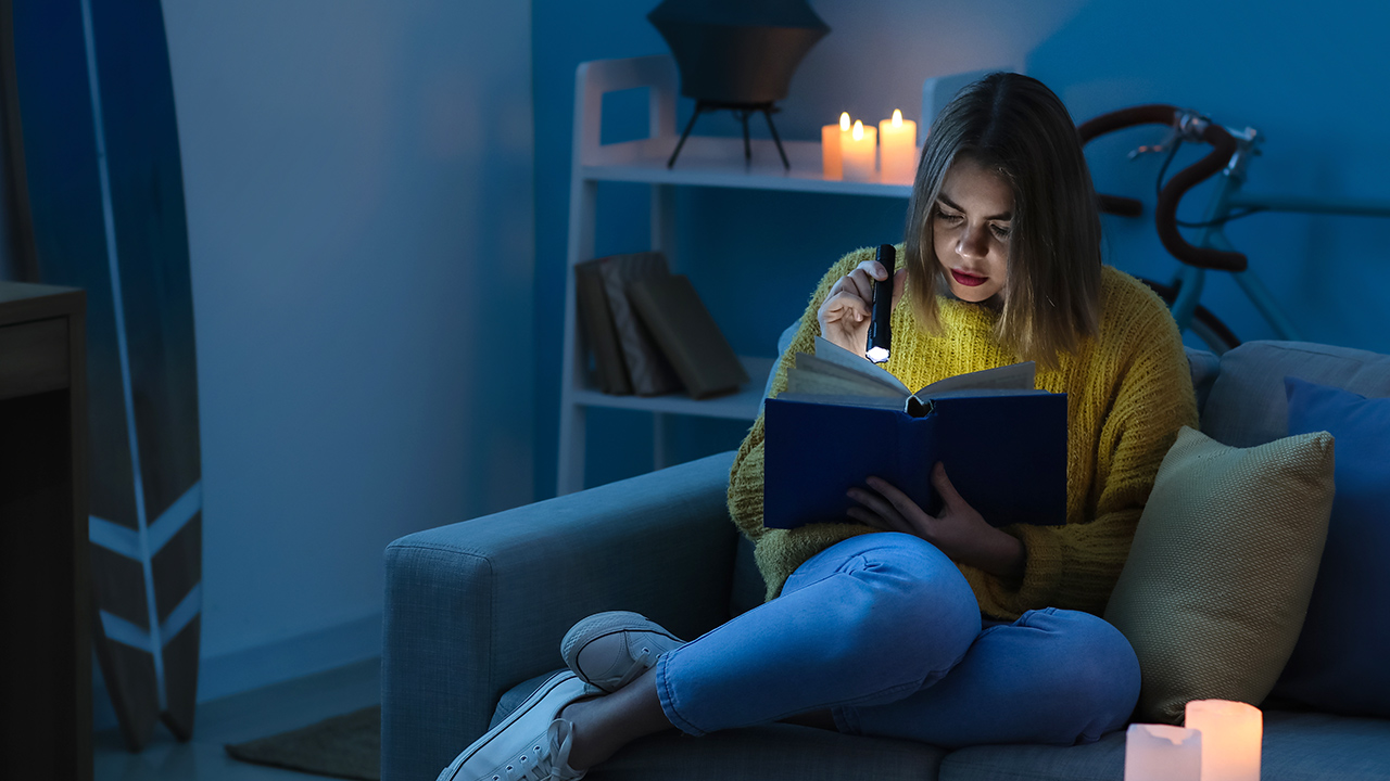 Chica leyendo a la luz de una linterna durante un apagón
